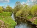 Ein idyllischer Panke Wanderweg schlängelt sich durch üppiges Grün. Ein kleiner Fluss fließt friedlich, gesäumt von Bäumen und Wiesen.