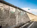 Beim Berlin Mauer besichtigen sieht man Graffiti und einen Heißluftballon.
