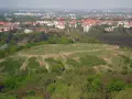 Blick vom Aussichtspunkt Drachenberg auf eine grüne Hügellandschaft mit Spaziergängern und der Stadt im Hintergrund.