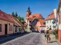 Frau mit Strohhut schlendert durch eine malerische Gasse mit Kopfsteinpflaster und roten Ziegeldächern. Ein besonderes Flair in Berlin.