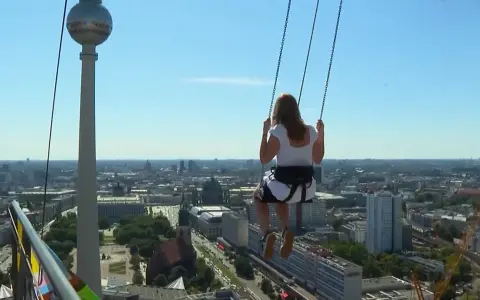Frau schaukelt hoch über Alexanderplatz Berlin, mit Blick auf die Stadt und den Fernsehturm.