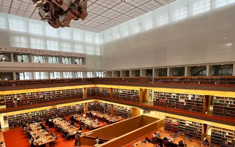 Große Bibliothek mit vielen Regalen voller Bücher. Menschen sitzen an Tischen und lesen. Ein Ort für Lesungen in Berlin.