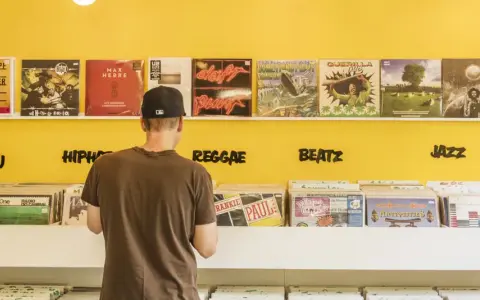 Mann durchstöbert Schallplatten in einem bunten Plattenladen in Berlin. Musikgenres wie HipHop, Reggae, Beatz und Jazz sind angeschrieben.