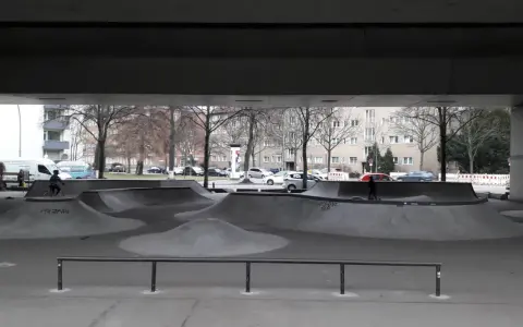 Ein leerer Berlin Skatepark unter einer Brücke. Ein Radfahrer fährt durch die Betonlandschaft.