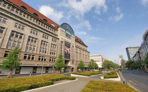 Das KaDeWe Berlin, ein imposantes Gebäude mit vielen Fenstern, steht unter einem blauen Himmel mit Wolken.