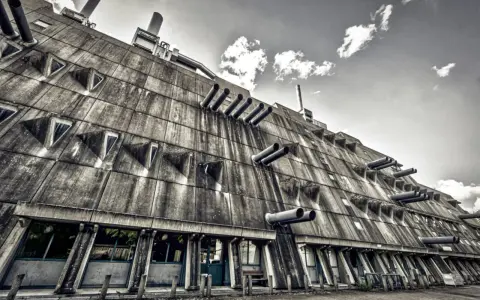 Betonriese im **Brutalismus Berlin**: Eine Fassade mit dreieckigen Fenstern und Rohren, die wie Kanonen aussehen.