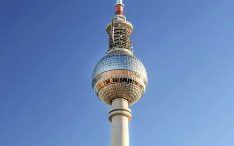 Die Torre della televisione di Berlino ragt in den blauen Himmel. Ihre kugelförmige Spitze mit Fenstern reflektiert das Licht.
