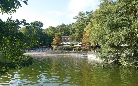 Grüne Bäume säumen den Schlachtensee Berlin, wo Menschen auf der Terrasse eines Restaurants sitzen.