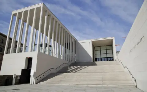 Moderne berlin architektur: James-Simon-Galerie mit langer Treppe und Säulengang vor blauem Himmel.