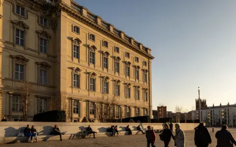 Sonnenlicht beleuchtet das barocke Gebäude, ein schönes Beispiel für kostenlose Orte, die man in Berlin besuchen kann. Menschen entspannen sich auf einer Bank.