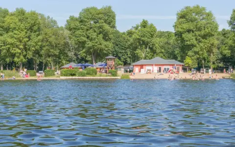 Sommerfreuden am See in Berlin: Menschen planschen im Wasser, entspannen am Strand und genießen die Sonne.