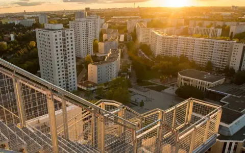 Blick von einer Treppe auf den Skywalk Marzahn bei Sonnenuntergang. Hohe Wohnhäuser und grüne Flächen prägen die Szenerie.