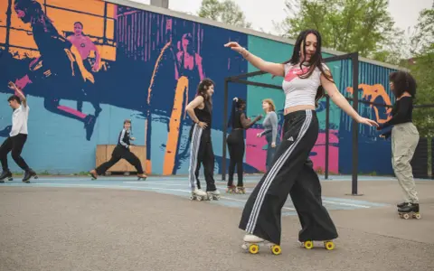 Eine Gruppe junger Leute genießt das Roller-Skating in Berlin vor einer bunten Wandmalerei.