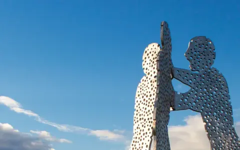 Der Molecule Man in Berlin, eine Skulptur aus Metall mit vielen Löchern, ragt gegen einen blauen Himmel mit Wolken.