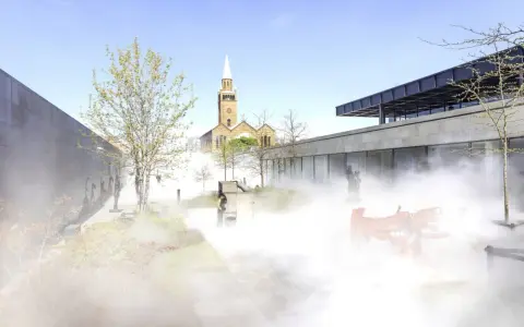 Ein nebliger Garten mit Skulpturen und einer Kirche im Hintergrund, ein friedlicher Ort für Christi Himmelfahrt in Berlin.