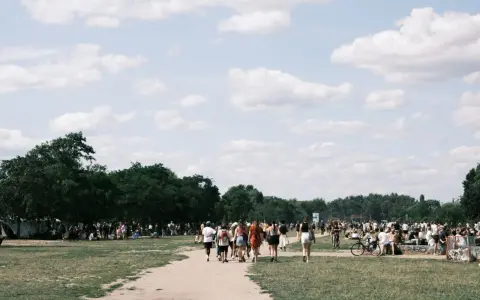 Menschen spazieren an einem sonnigen Pfingstmontag in Berlin durch eine grüne Parklandschaft.