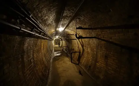 Dunkler, feuchter Ziegelgang in den Berliner Katakomben, Rohre verlaufen an der Decke, ein Lichtschein in der Ferne.