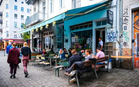 Menschen sitzen an Tischen vor einem **Prenzlauer Berg Restaurant** mit türkisfarbener Markise und Graffiti.