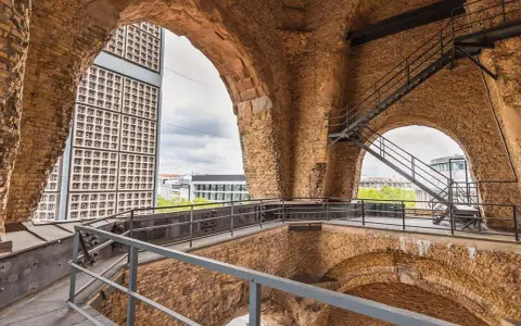 Blick durch die Bögen der Kaiser-Wilhelm-Gedächtniskirche auf eine moderne Glasfassade und Treppen.