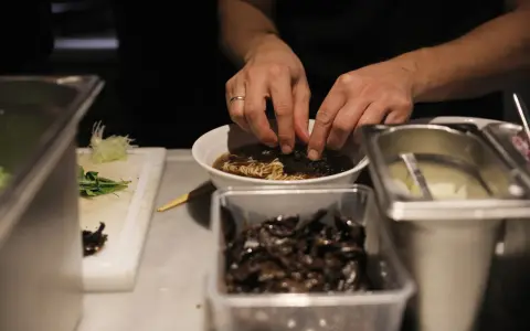 Hände garnieren eine Schüssel mit Ramen-Nudeln in Berlin. Daneben liegen Zutaten bereit.