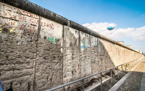 Beim Berlin Mauer besichtigen sieht man Graffiti und einen Heißluftballon.