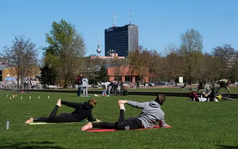Menschen machen Yoga und entspannen sich im Park. Ein sonniger Tag für Sport in Berlin mit dem Fernsehturm im Hintergrund.