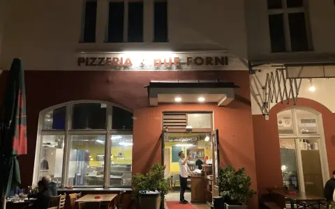 Abendstimmung vor der Pizzeria "Due Forni". Ein Mann steht im Eingangsbereich, während Gäste an Tischen im Freien sitzen.