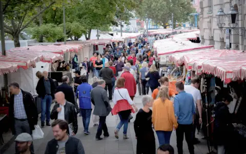 Menschen schlendern über einen belebten kunstmarkt berlin mit vielen Ständen und bunten Markisen.