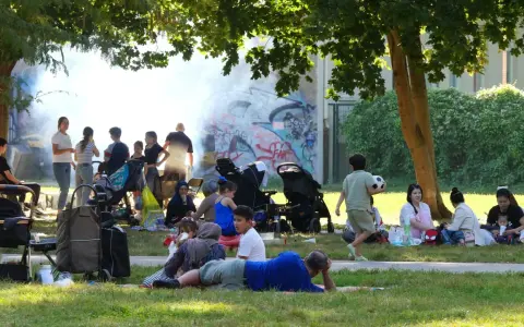 Familien genießen den Sommer auf einem Grillplatz in Berlin. Rauch steigt von einem Grill auf, während Kinder spielen und sich entspannen.