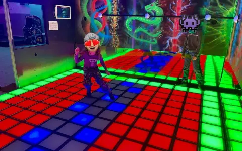 Kinder spielen im **underground lasergame Berlin** auf einer leuchtenden Tanzfläche. Bunte Drachen zieren die Wand.
