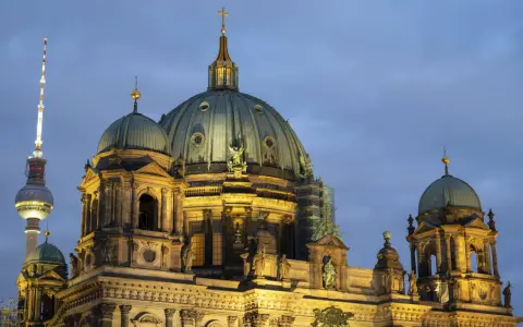 Prachtvolle Kuppeln des Berliner Doms im Abendlicht, mit dem Fernsehturm im Hintergrund. Ein Wahrzeichen der Kirchen in Berlin.