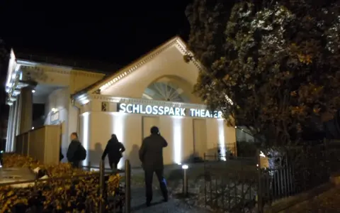 Abendliche Beleuchtung am **Schlosspark Theater**. Drei Personen nähern sich dem Eingang.