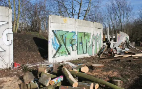 Graffiti-bemalte Überreste der Berliner Mauer, umgeben von Holzstapeln und Trümmern.