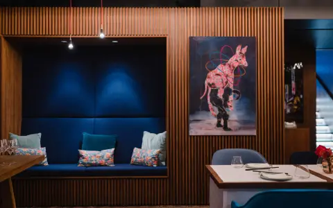 Gemütliche Nische mit blauen Kissen und einem orientalischen Teppich. Ein Kunstwerk mit einem pinken Zebra ziert die Holzwand. Ein echter Berlin Restaurant Geheimtipp.