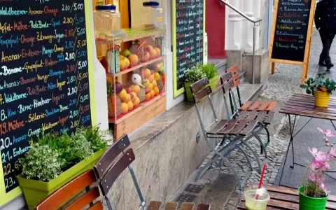 Frischer Smoothie in Berlin. Bunte Tafel mit Frucht- und Gemüsesorten, daneben leere Stühle und ein Tisch.