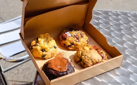 Vier köstliche, hausgemachte Cookies in einer Pappschachtel – die besten Cookies Berlins, bereit zum Genießen.