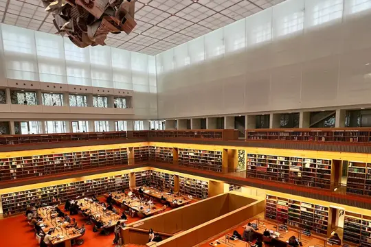 Große Bibliothek mit vielen Regalen voller Bücher. Menschen sitzen an Tischen und lesen. Ein Ort für Lesungen in Berlin.