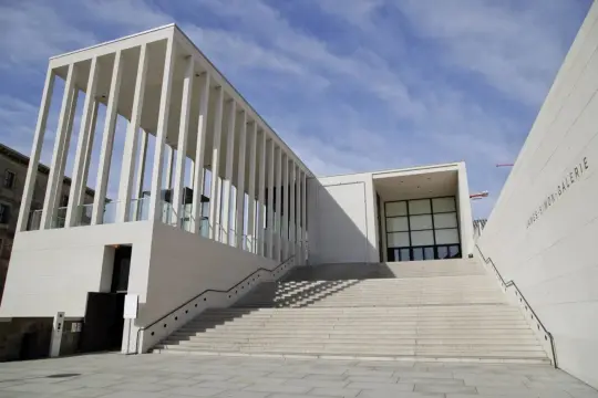 Moderne berlin architektur: James-Simon-Galerie mit langer Treppe und Säulengang vor blauem Himmel.