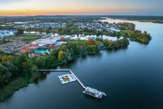 Luftaufnahme der Havel Therme mit einem schwimmenden Pool auf dem Wasser. Ein idyllisches Bild der Entspannung am See.
