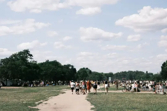 Menschen spazieren an einem sonnigen Pfingstmontag in Berlin durch eine grüne Parklandschaft.