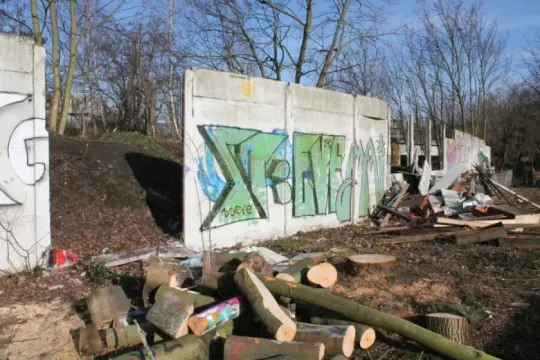 Graffiti-bemalte Überreste der Berliner Mauer, umgeben von Holzstapeln und Trümmern.