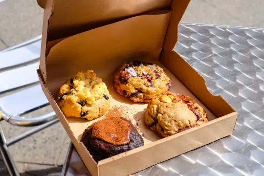 Vier köstliche, hausgemachte Cookies in einer Pappschachtel – die besten Cookies Berlins, bereit zum Genießen.