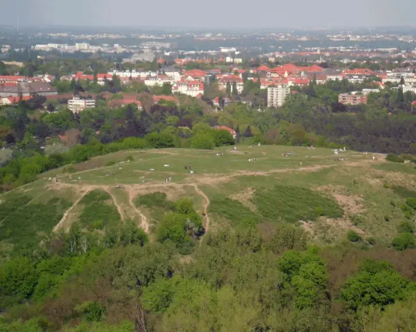 Blick vom Aussichtspunkt Drachenberg auf eine grüne Hügellandschaft mit Spaziergängern und der Stadt im Hintergrund.