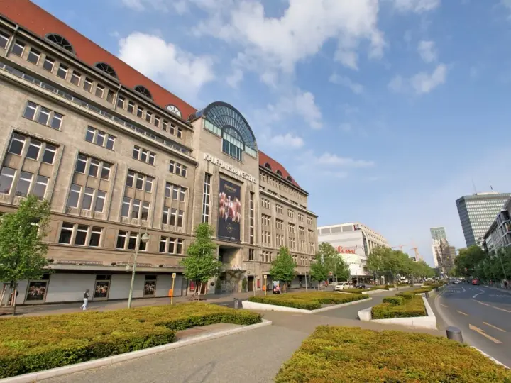 Das KaDeWe Berlin, ein imposantes Gebäude mit vielen Fenstern, steht unter einem blauen Himmel mit Wolken.