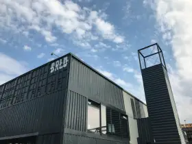 Moderne Containerarchitektur am **brlo gleisdreieck** mit Schriftzug "BALD" und einem markanten Turm unter blauem Himmel.