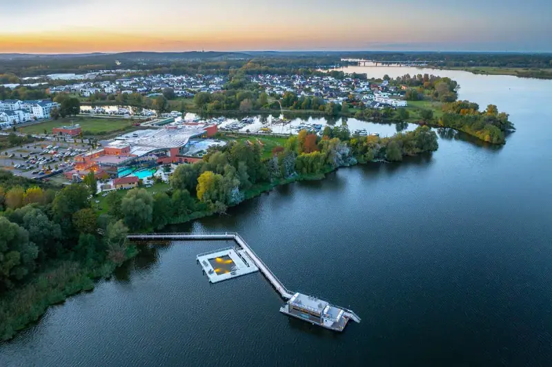 Luftaufnahme der Havel Therme mit einem schwimmenden Pool auf dem Wasser. Ein idyllisches Bild der Entspannung am See.