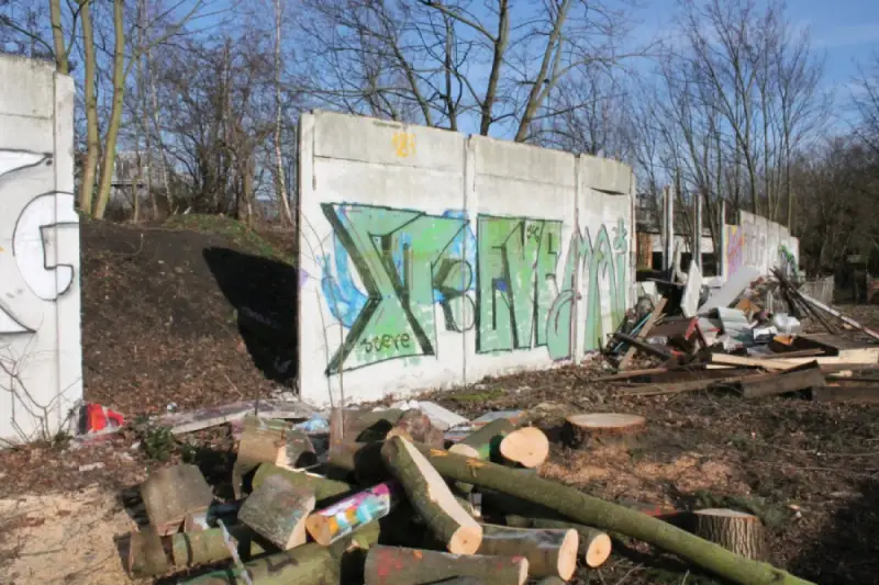 Graffiti-bemalte Überreste der Berliner Mauer, umgeben von Holzstapeln und Trümmern.